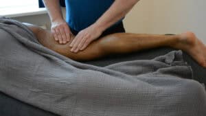 Een masseur kneedt het bovenbeen aan de achterkant