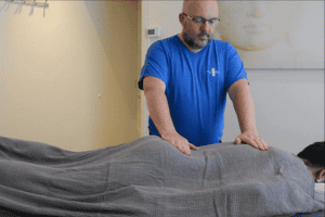 Een masseur legt zijn handen op het doek wat over een massageklant ligt. De start bij een veilige massage cursus